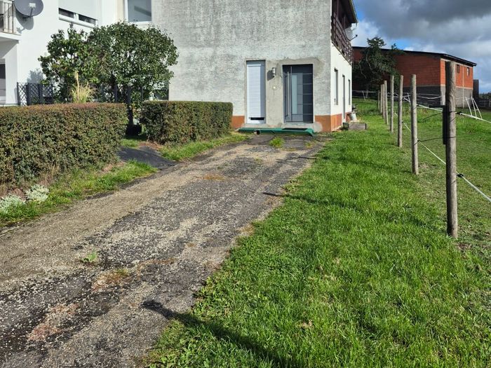 Giebelseite mit grauer Eingangstür zu Wohnung 1 und Zufahrt neben der Weide