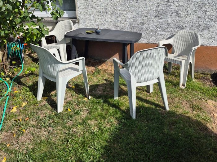 Gartentisch mit vier weißen Stühlen an der Hauswand bei Wohnung 1