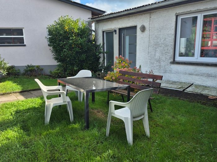 Glastisch mit weißen Stühlen und Bank auf dem Rasen bei Wohnung 2